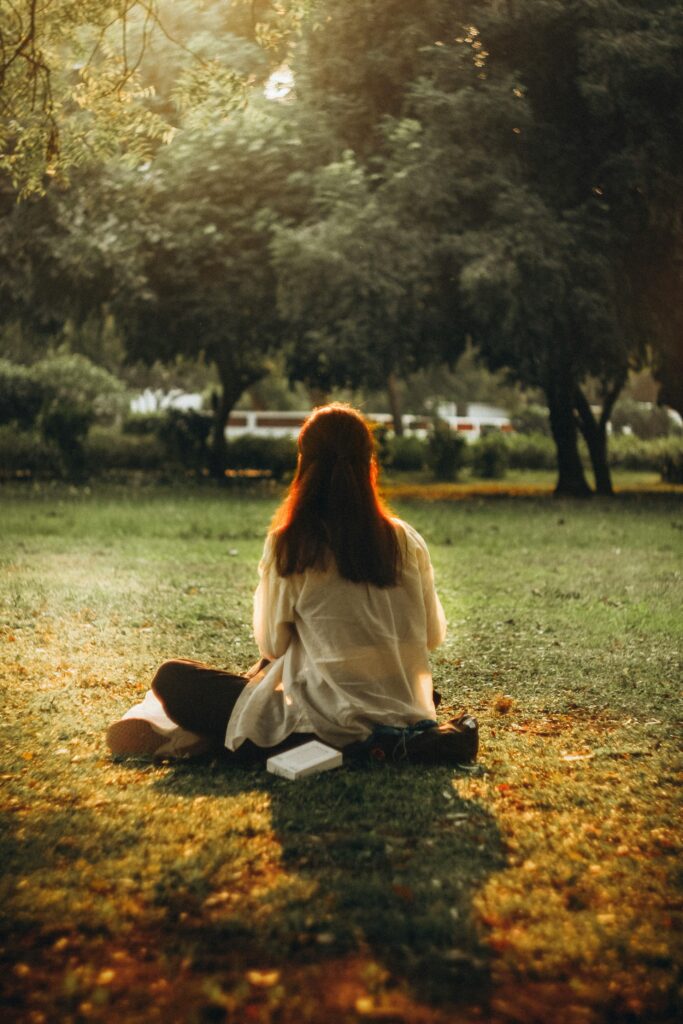 Young woman enjoys a peaceful moment seated on grass in a sunlit park.